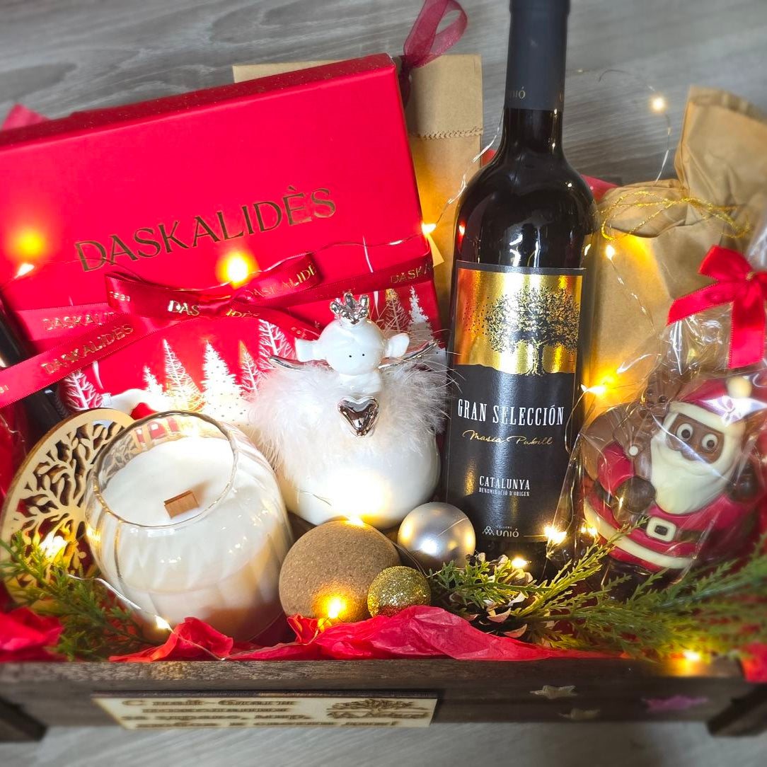 Gift basket with chocolate box Daskalidès,  wine bottle, candles, and decorative items on a wooden surface.